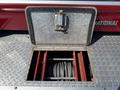 A metal storage compartment with a hinged lid is open revealing two red sections inside and a spool of wire rope at the bottom