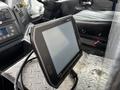A touchscreen display mounted on a dashboard with buttons and controls visible in the background