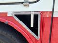 A metal access panel with a triangular shape is attached to a red vehicle with a black tire visible in the foreground