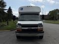 A 2013 Chevrolet Express with a white body and a raised roof featuring a blue handicap symbol on the front. The vehicle has side mirrors and a silver bumper