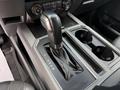 Close-up of the gear shift lever in a 2019 Ford F-150 truck showing P R N D M settings with a leather boot and console cup holders