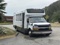 A 2020 Chevrolet Express van with a white exterior and black accents parked at an angle, featuring large windows and a high roof designed for passenger transport