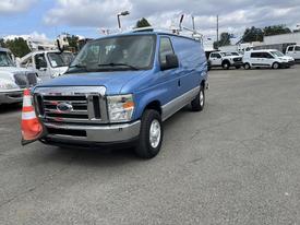 A blue 2009 Ford Econoline van with a silver stripe and a traffic cone attached to the front grille