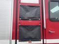 Two black canvas storage compartments mounted on the side of a red fire truck with silver detailing