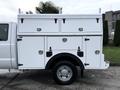 A 2015 Ford F-350 SD with a white utility bed featuring multiple storage compartments and metal handles on the side