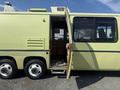 A 1976 GMC Motorhome in a light green color with an open door revealing an interior that includes wooden paneling and visible flooring