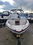 A 2013 Larson 238 boat with a white and black exterior and a red stripe at the bow is parked on a trailer in a marina setting
