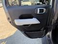 A close-up view of the driver's side door panel of a 2021 Jeep Gladiator featuring a gray handle and armrest with a textured black interior surface and storage netting
