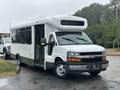 A white 2018 Chevrolet Express bus with a large front windshield and door open, designed for passenger transport