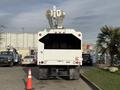 A white 2011 International 4300 bucket truck with extended lift arms positioned at the rear facing a traffic cone
