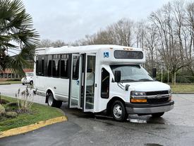 A 2013 Chevrolet Express bus with a white exterior and an open door displaying a wheelchair symbol