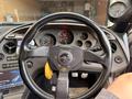 A close-up view of the steering wheel and dashboard of a 1997 Toyota Supra featuring a black steering wheel with a yellow shift knob and various gauges visible