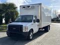 A white 2023 Ford E-450 box truck with a refrigeration unit on top parked with a clear view of the front and side
