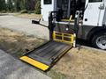 A 2020 Chevrolet Express with a wheelchair accessibility lift extended featuring yellow safety markings and a textured surface for grip
