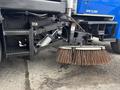 A 2013 International DuraStar 4300 street sweeper with a large rotating broom attachment in the foreground