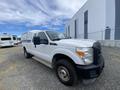 A 2014 Ford F-350 SD truck with a white exterior and a cargo area cover parked at an industrial location