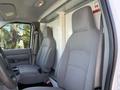 Interior of a 2023 Ford E-450 showing two gray cloth seats in the driver's cabin with a simple dashboard and a white partition behind the seats