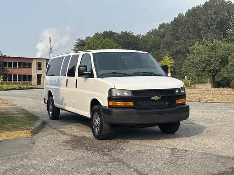 A white 2021 Chevrolet Express van with a black front grille and wheels parked on a gravel surface