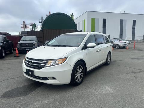 A 2015 Honda Odyssey in white with a sleek design and alloy wheels parked at a location with several other vehicles in the background