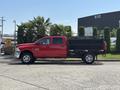 A red 2013 RAM 2500 pickup truck with a flatbed and black metal storage box on the back is parked with palm trees nearby
