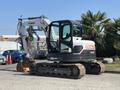 A 2010 Bobcat E80 compact excavator with a white and black exterior tracks and an articulated arm with a bucket attachment