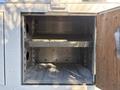 An open compartment of a 2006 Freightliner M2 106 with two metal shelves and a clean interior devoid of any items