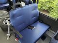 A blue bench seat with a padded backrest and seat cushion is secured inside a vehicle with seatbelts visible and a wheel partially seen in the background