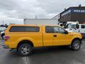 A bright yellow 2014 Ford F-150 pickup truck with a truck cap and chrome wheels is shown from the side