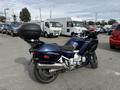 A blue 2016 Yamaha FJR1300AE motorcycle with a rear top case situated on a parking lot surrounded by various vehicles
