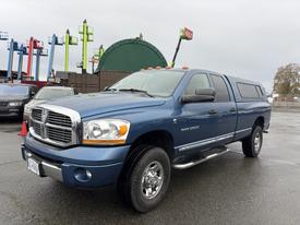 A blue 2006 Dodge Ram 2500 pickup truck with a camper shell and chrome wheels is parked in a lot