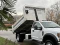 A 2021 Ford F600 dump truck with its bed raised, showcasing a large metallic truck bed designed for transporting materials
