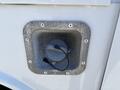 Close-up of a round fuel access port with a gray cap and two black wires attached on a white surface