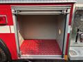 An empty compartment of a 1999 Freightliner FL80 fire truck with a red grid floor and a circular opening on the side