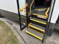 A 2020 Chevrolet Express bus with an open door reveals a set of yellow steps leading inside the vehicle with safety warnings posted on the step edges