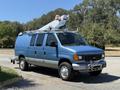 A blue 2006 Ford Econoline van with a rooftop ladder and equipment mounts parked on a street