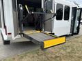 A 2014 Ford E-350 with a lift ramp extended from the rear door designed for accessibility featuring yellow and black components