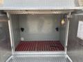 Interior view of a storage compartment in a 1999 Freightliner FL80 with a red grid floor and metal walls featuring two pipe connections and a light fixture