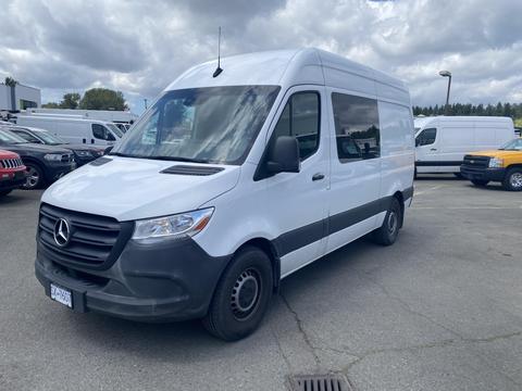A 2022 Mercedes-Benz Sprinter van in white with a black stripe on the lower section and black wheels parked at a commercial location