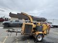 A yellow 2015 Vermeer Corporation BC1200XL wood chipper with a large chute and wheels designed for landscaping and tree maintenance work
