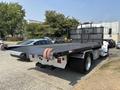 A 2020 Peterbilt 330 tow truck with a flatbed and dual rear wheels parked beside cars