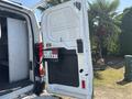 A white 2019 Ford Transit 350 with an open rear door showing interior shelving and mounted equipment on the door