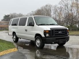 A 2013 Ford E-350 van in white with a black grille facing forward and parked on a wet surface