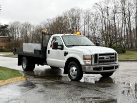 A white 2008 Ford F-350 pickup truck with a flatbed and tool storage compartment and amber lights on the roof