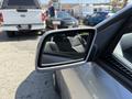 A side mirror of a 2004 BMW 6-Series reflecting a blurred view of a gray vehicle and a person in a blue shirt standing nearby