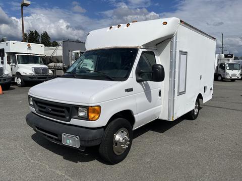 A white 2004 Ford Econoline with a boxy cargo area and front passenger doors is parked, featuring large wheels and a simple design