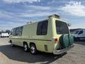 A 1976 GMC Motorhome in a pale yellow hue with a rounded body design and two green spare tire covers mounted at the rear