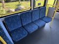 A row of blue patterned seats inside a bus with yellow handrails and accessible signs visible on the bus walls