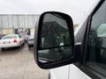 A 2021 Chevrolet Express side mirror with raindrops on its surface reflecting the surrounding areas