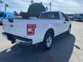 A white 2018 Ford F-150 pickup truck is parked, featuring a short bed with a rugged design and chrome detailing on the rear bumper and tailgate