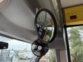 A round rearview mirror reflecting the interior of a bus with yellow seating and a small fan mounted nearby